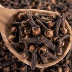 Cengkeh kering di atas sendok kayu dengan latar rempah alami.