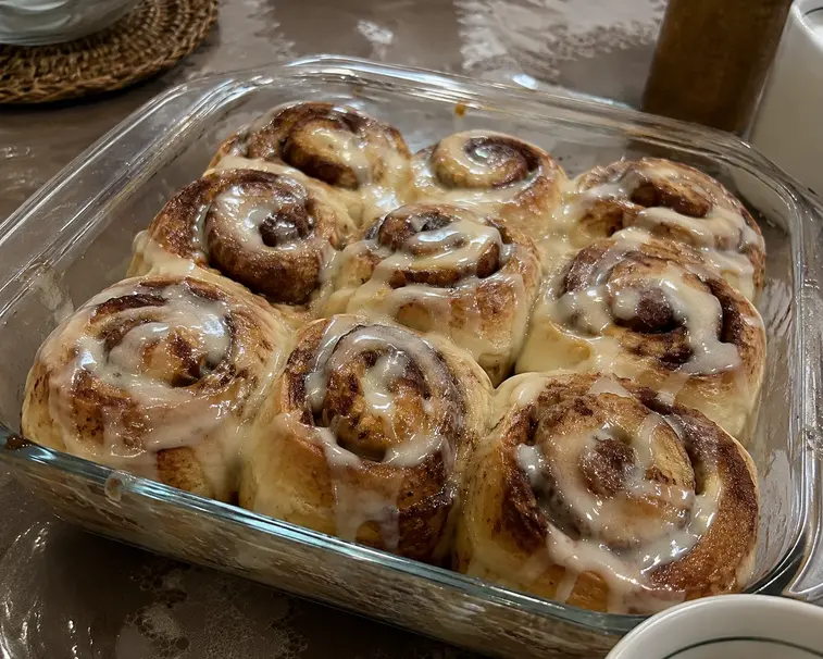 Cinnamon roll lembut dengan topping glaze manis dan taburan kayu manis dalam loyang kaca