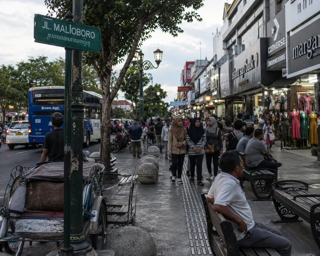 Suasana Jalan Malioboro Yogyakarta dengan papan nama Malioboro, becak, wisatawan, dan pusat perbelanjaan