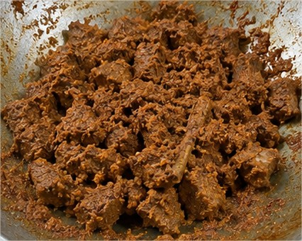 Proses memasak rendang daging sapi khas Padang di dalam wajan besar hingga bumbu rempah meresap dan mengering.