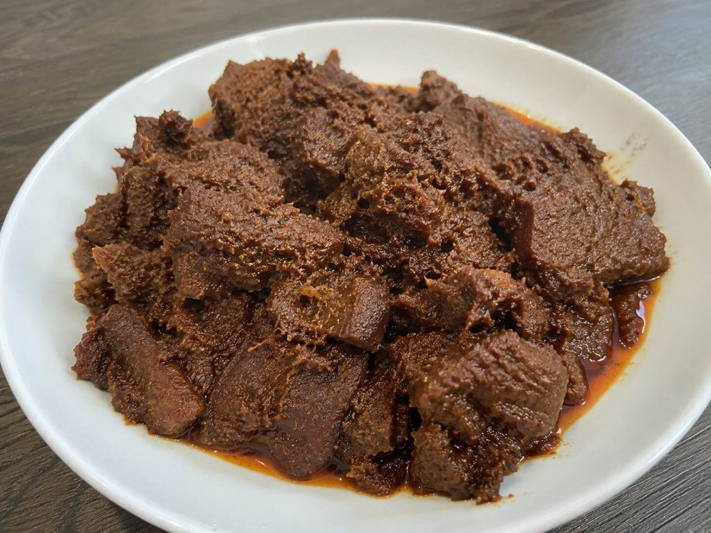 Rendang daging sapi Padang asli dengan bumbu rempah khas Minangkabau yang meresap, disajikan di atas piring putih.