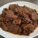 Rendang daging sapi Padang asli dengan bumbu rempah khas Minangkabau yang meresap, disajikan di atas piring putih.