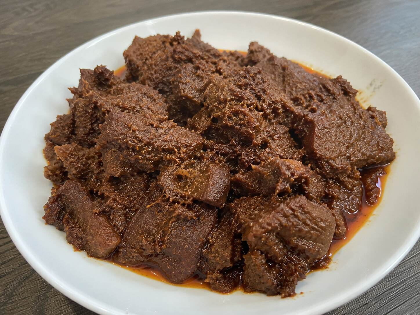 Rendang daging sapi Padang asli dengan bumbu rempah khas Minangkabau yang meresap, disajikan di atas piring putih.
