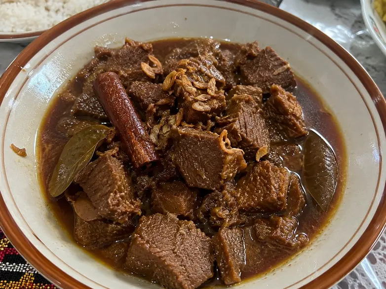 Semur daging sapi dengan batang kayu manis dan bumbu rempah khas Indonesia dalam mangkuk saji