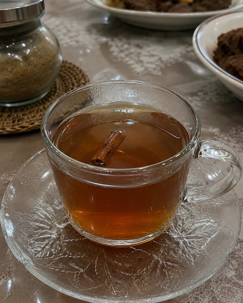 Teh kayu manis hangat dalam cangkir kaca dengan batang kayu manis alami sebagai minuman herbal