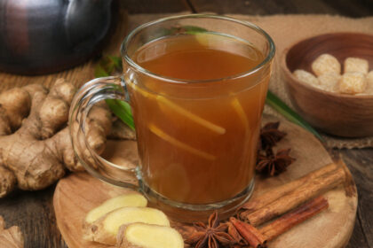 Segelas minuman bandrek khas Sunda hangat dengan jahe segar, kayu manis, bunga lawang, dan gula aren di atas meja kayu.