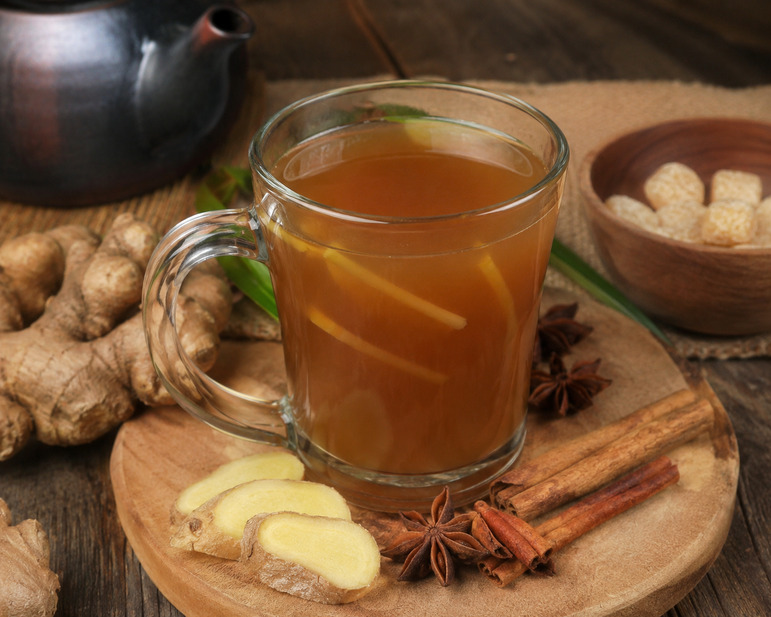 Segelas minuman bandrek khas Sunda hangat dengan jahe segar, kayu manis, bunga lawang, dan gula aren di atas meja kayu.