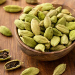Buah kapulaga hijau utuh dan biji kapulaga dalam mangkuk kayu sebagai rempah aromatik untuk masakan dan minuman.