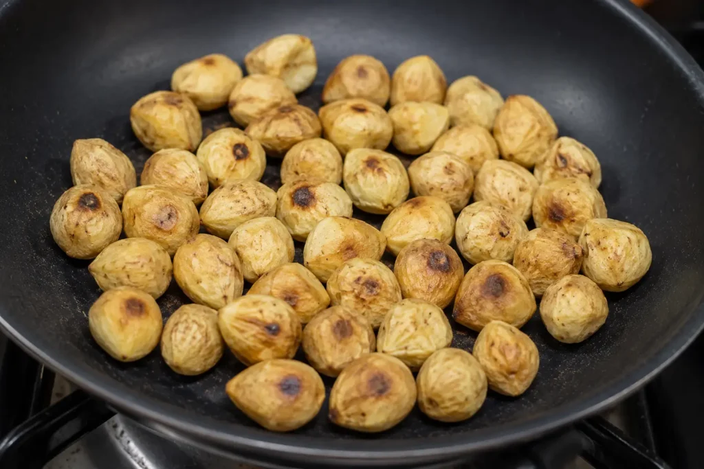 Kemiri sedang disangrai di atas wajan hingga berwarna keemasan untuk menghasilkan aroma gurih sebelum dijadikan bumbu masakan.