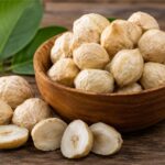 Biji kemiri utuh dan belahan kemiri di dalam mangkuk kayu sebagai bumbu dapur alami khas Indonesia.