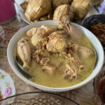 Opor ayam kuah santan gurih siap disajikan dengan taburan bawang goreng, ketupat, dan sambal khas menu Lebaran.