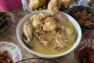 Opor ayam kuah santan gurih siap disajikan dengan taburan bawang goreng, ketupat, dan sambal khas menu Lebaran.
