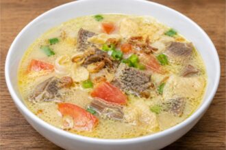 Semangkuk Soto Betawi khas Jakarta dengan kuah santan gurih, potongan daging sapi, tomat, daun bawang, bawang goreng, dan emping.
