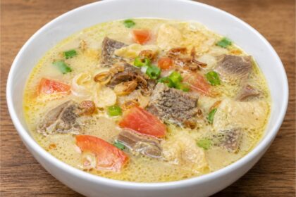 Semangkuk Soto Betawi khas Jakarta dengan kuah santan gurih, potongan daging sapi, tomat, daun bawang, bawang goreng, dan emping.