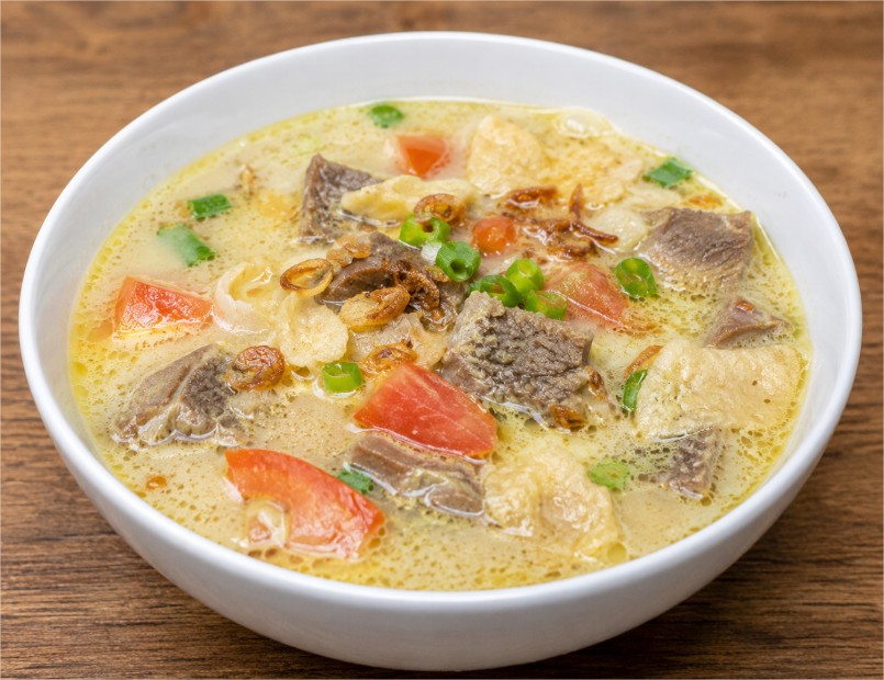 Semangkuk Soto Betawi khas Jakarta dengan kuah santan gurih, potongan daging sapi, tomat, daun bawang, bawang goreng, dan emping.