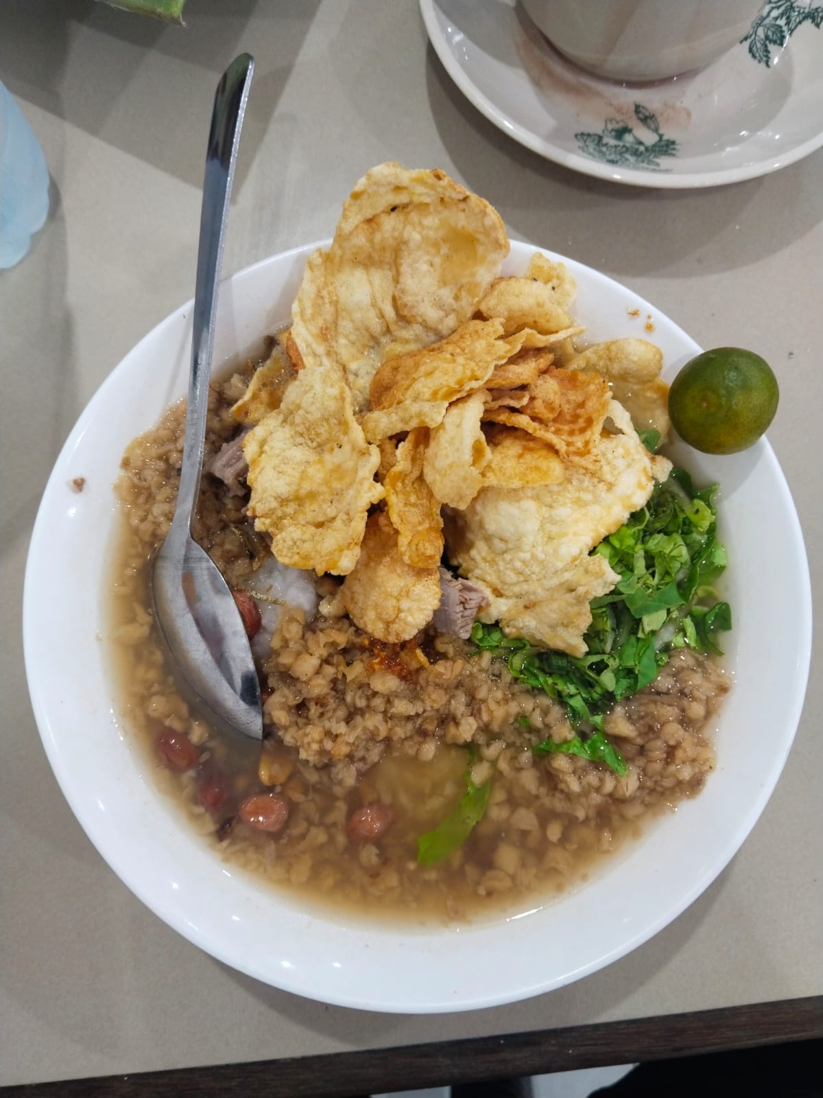 Bubur Pekong khas Singkawang dengan daging sapi, kerupuk goreng, kacang, daun bawang, dan jeruk limau dalam kuah kaldu gurih