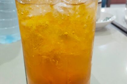 Es Nammong khas Singkawang berwarna kuning keemasan disajikan dalam gelas tinggi dengan es batu, tampak segar dan dingin di atas meja restoran.